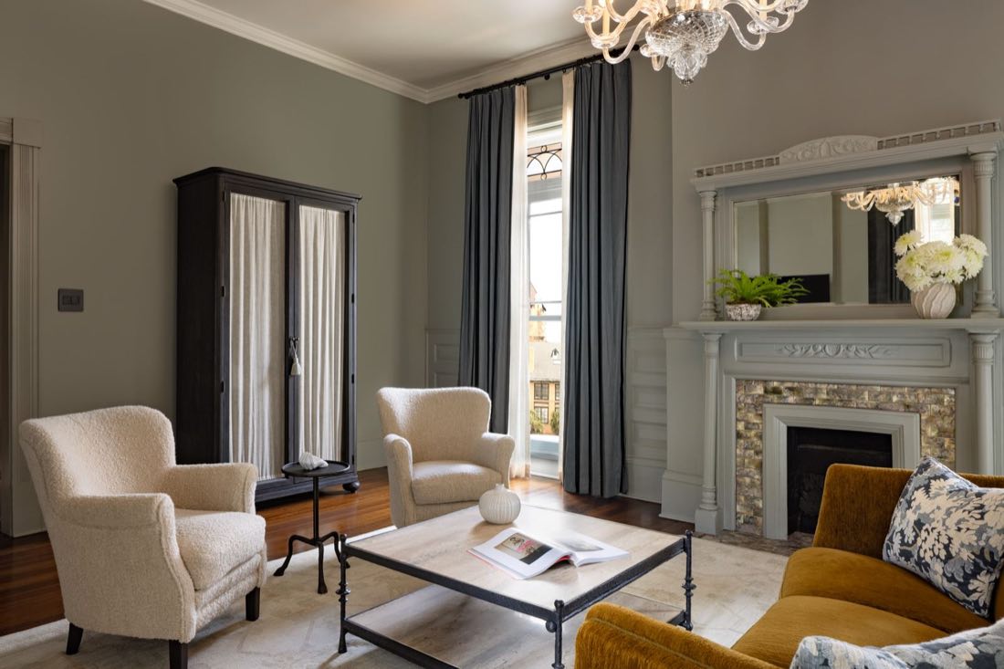 The sitting area in Room Five, a black armoire and cream wing chairs by a mirrored mantel.