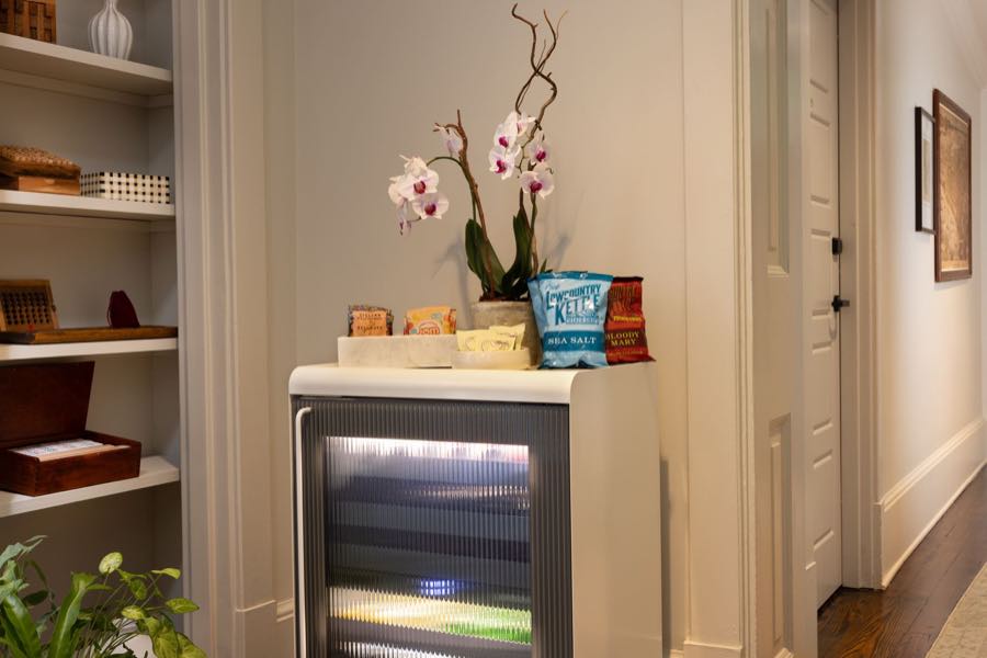 The floor pantry alcove, an orchid and snacks beside a glass-front beverage fridge.