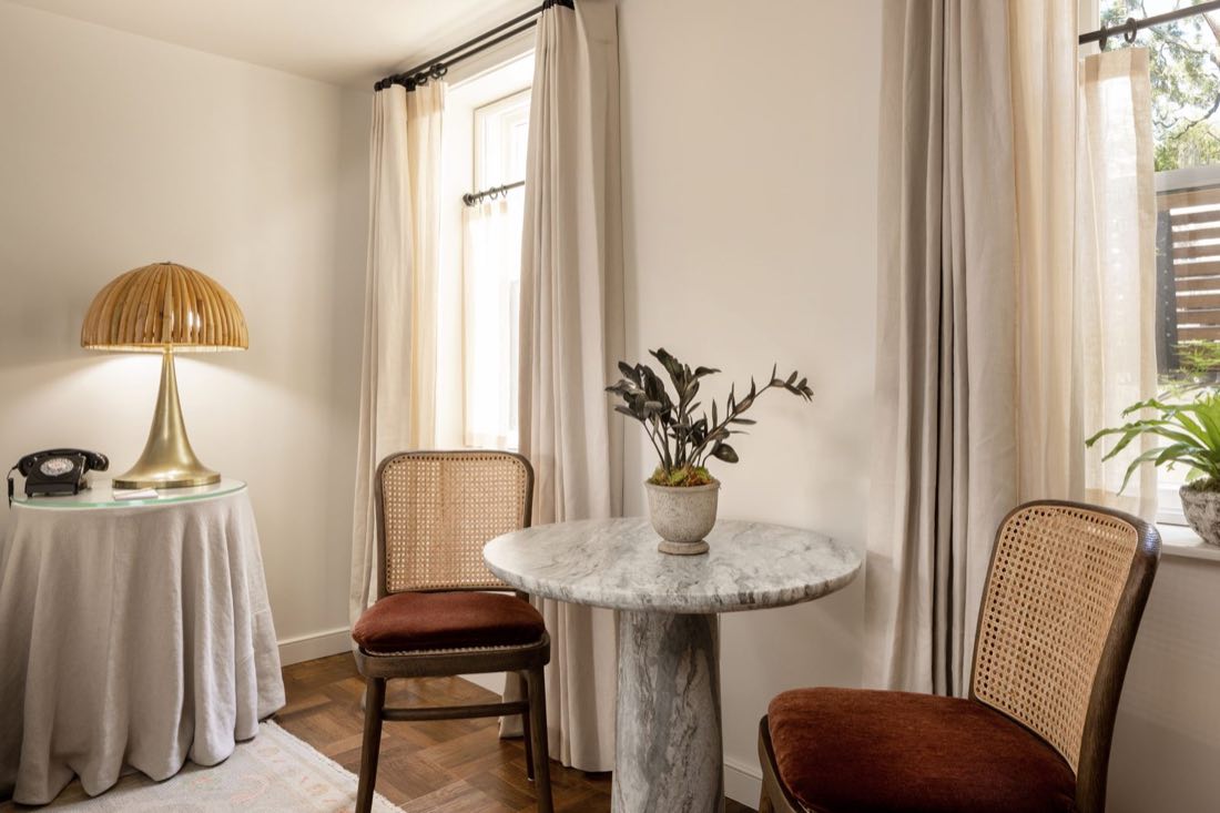 The seating corner in Room Four, rattan chairs at a marble bistro table on a herringbone floor.