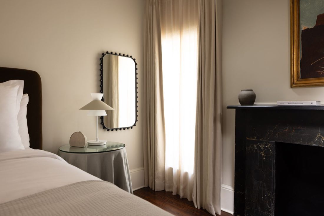 Room Twelve, a scalloped mirror above a black marble mantel, a dome lamp at the sheer curtain.