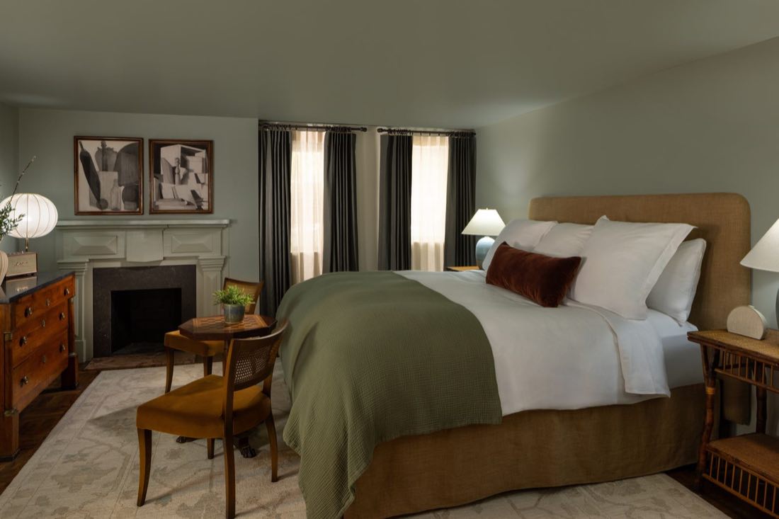 Room Three, sage walls and a tan upholstered bed under a white mantel and paired cubist prints.