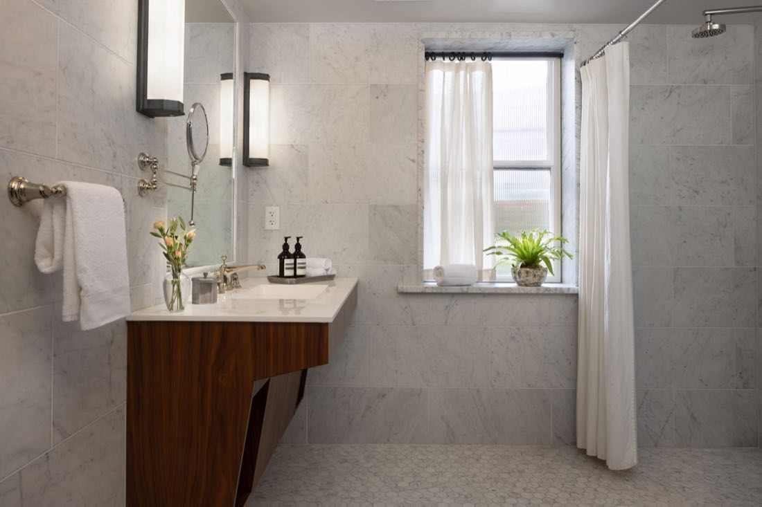 The bathroom in Room Four, a walnut vanity and marble beside a curtained tub and shower.