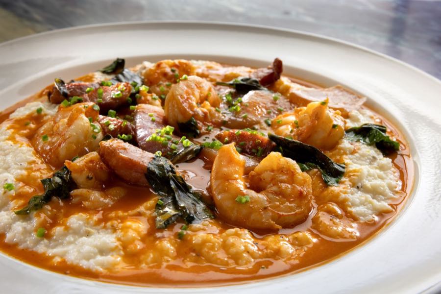 Lowcountry shrimp and grits close in, shrimp and sausage in tomato broth under fried basil.