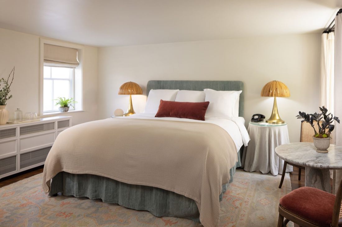Room Four, our accessible room, a sage bed with brass dome lamps and a skirted side table.